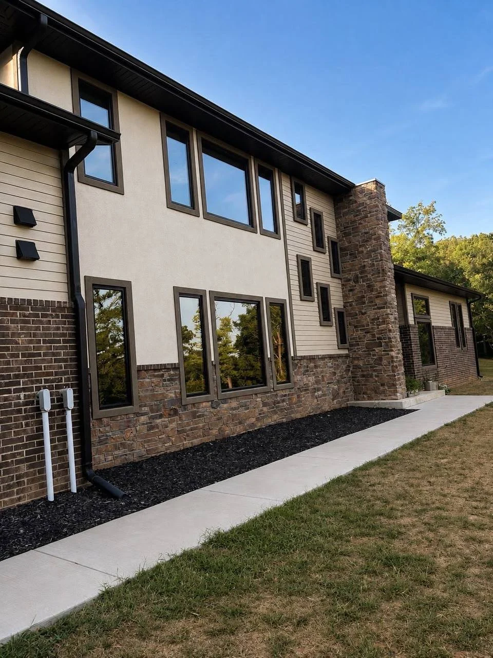 Modern two-story home exterior with large windows, stone chimney, brick accents, and concrete walkway